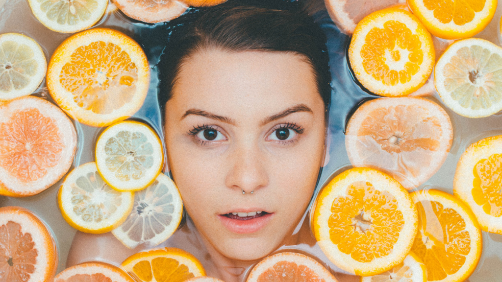 C-vitamin som hjälper mot rynkor. Kvinnligt ansikte syns i ett bad med skivad citrusfrukt.