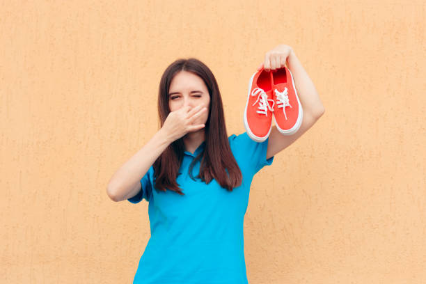 Kvinna håller för näsan och håller upp ett par illaluktande skor