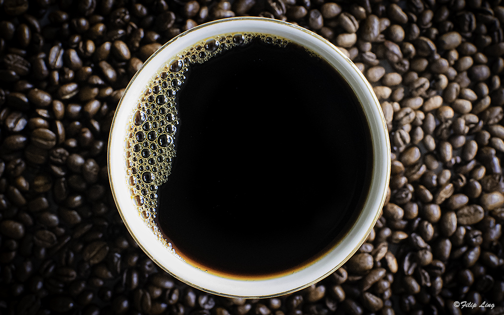 Vad är kaffets historia? kaffekopp med svart kaffe och bönor runt om