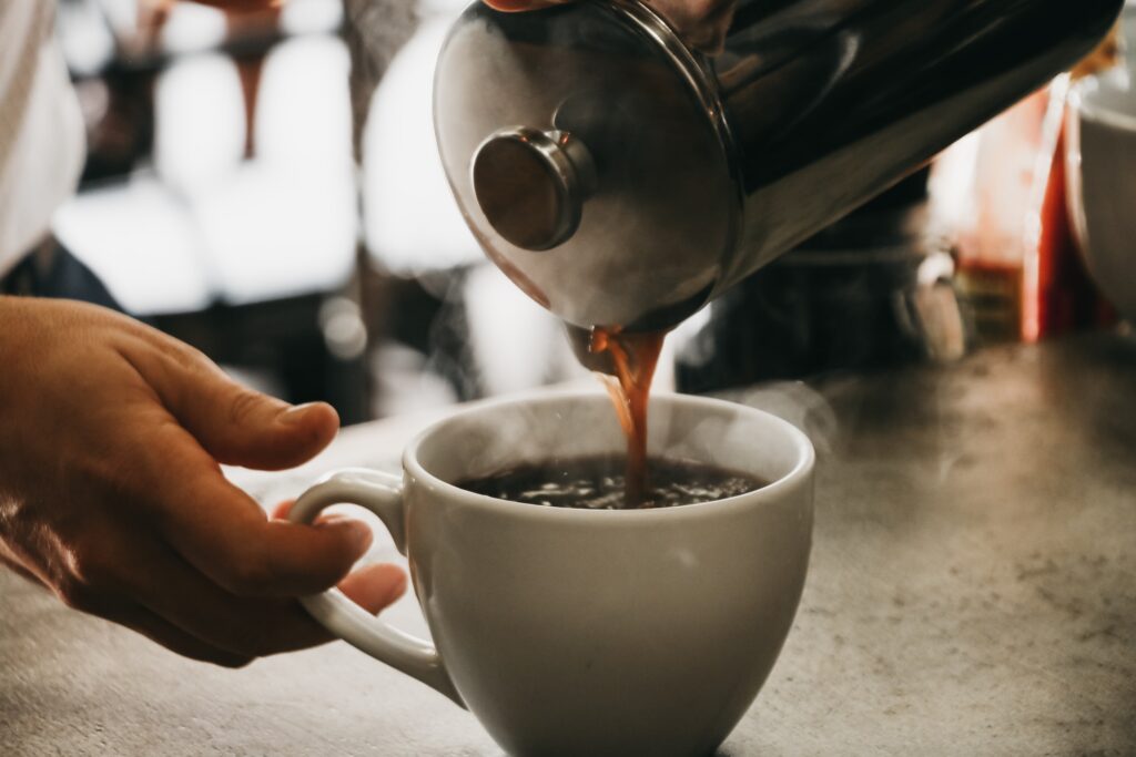 Rykande kaffe hälls i en vit kopp från en presskanna. 