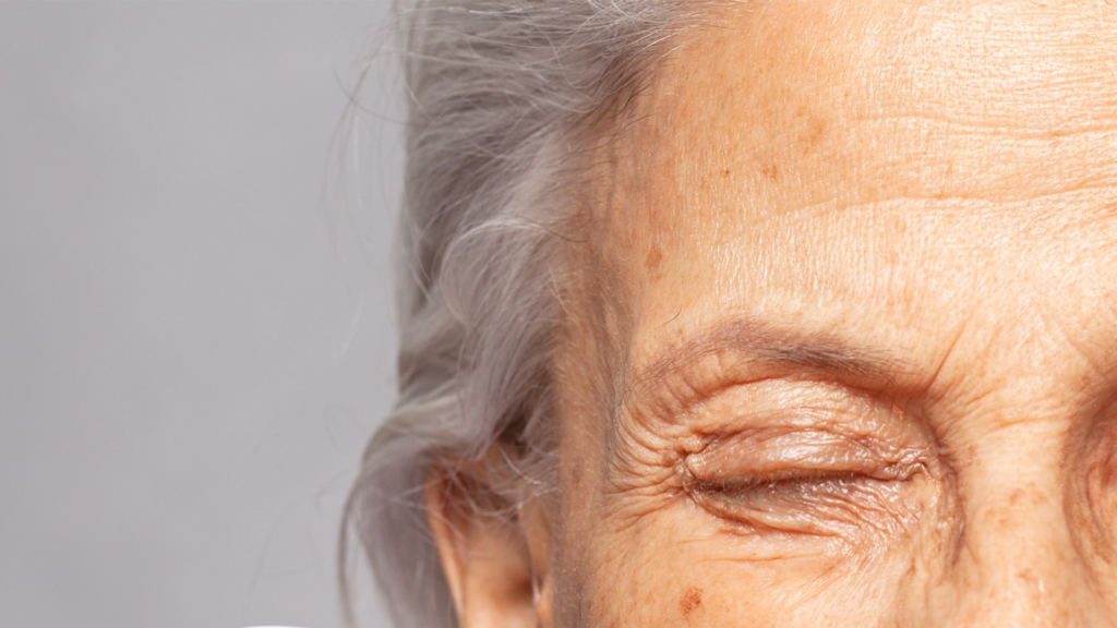 Äldre kvinna med grått hår och rynkor som blundar.